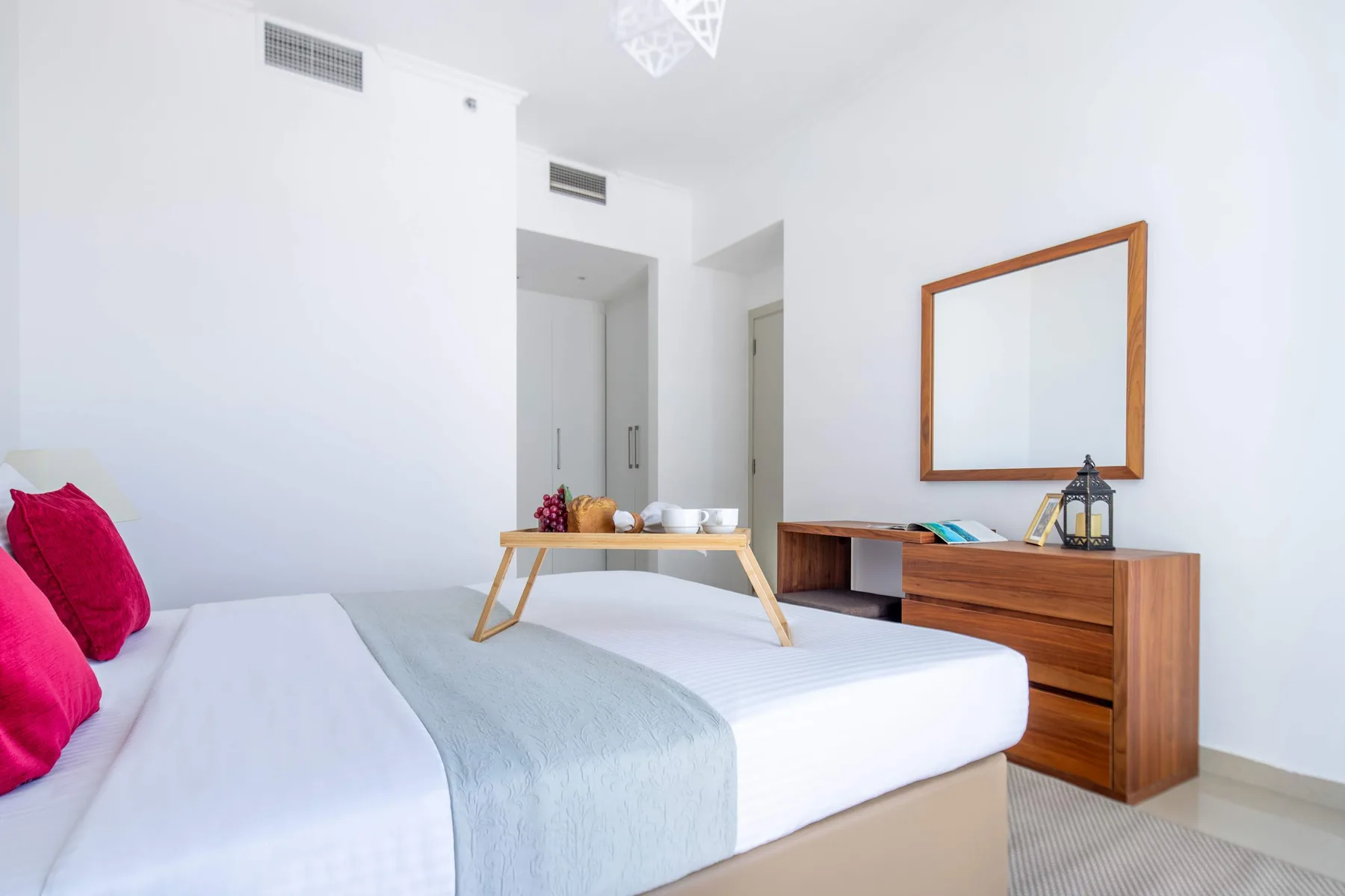 A bright bedroom with a bed, wooden dresser, and mirror.