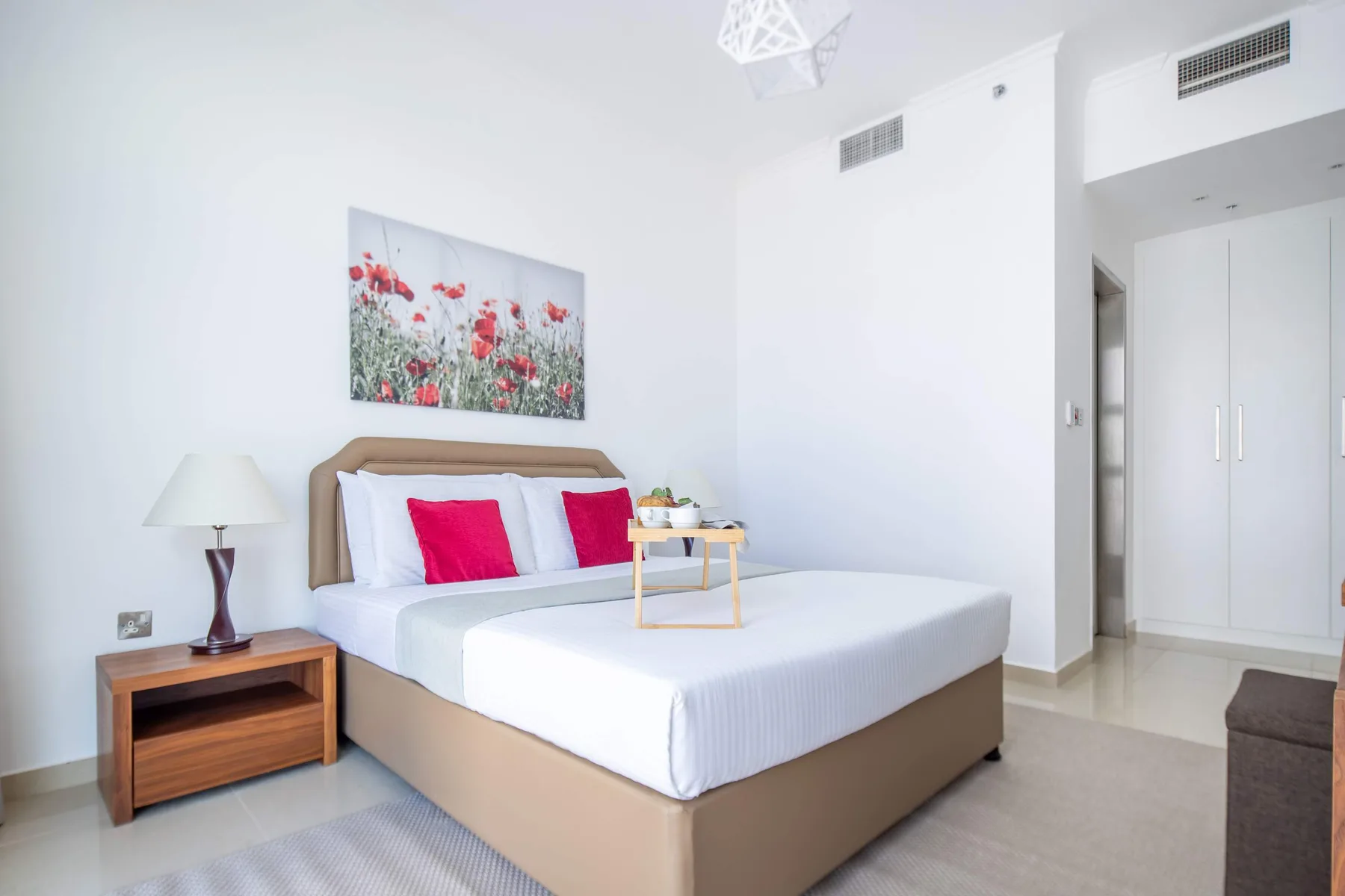 A bright bedroom with a neatly made bed and floral wall art.