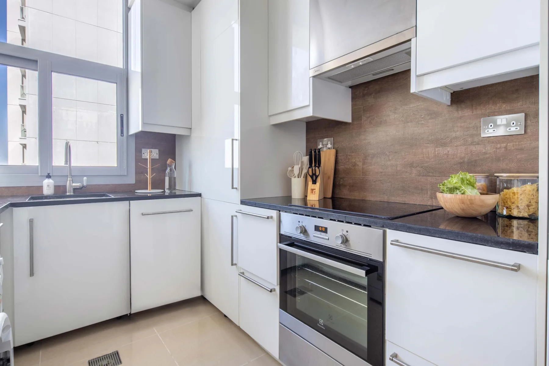 A bright kitchen with white cabinets, a dark countertop, and an oven.