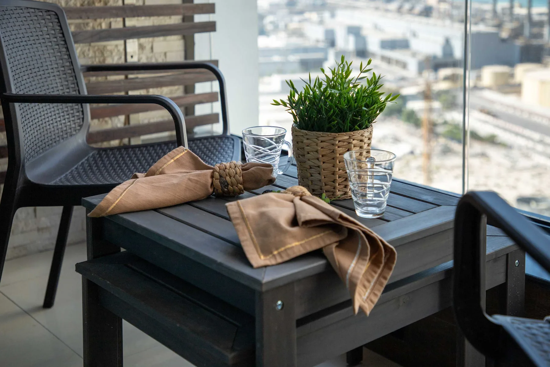 A balcony seating area with a dark table, glasses, and a potted plant.