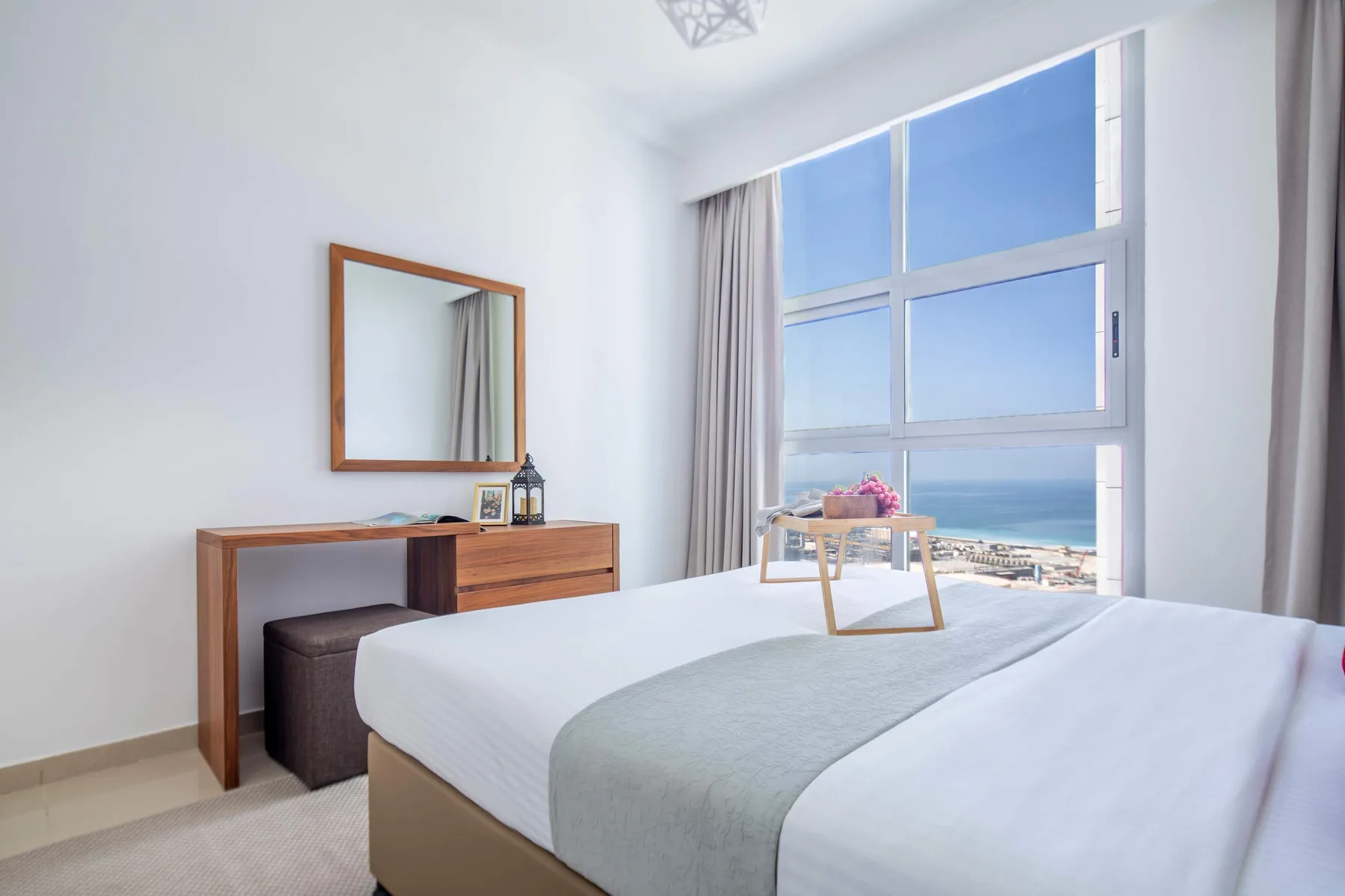 A bright bedroom with a neatly made bed and large windows overlooking the sea.