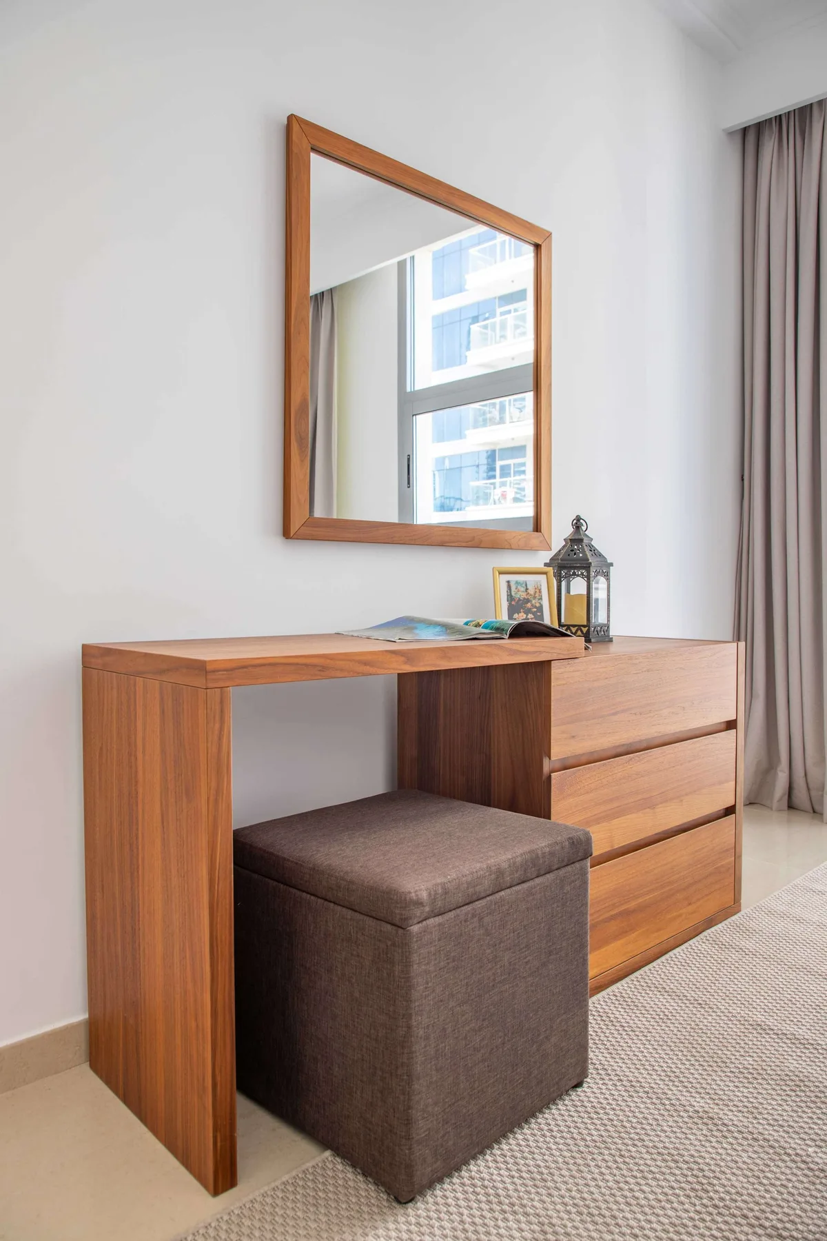 A wooden dressing table with a cushioned stool sits beneath a wall mirror.