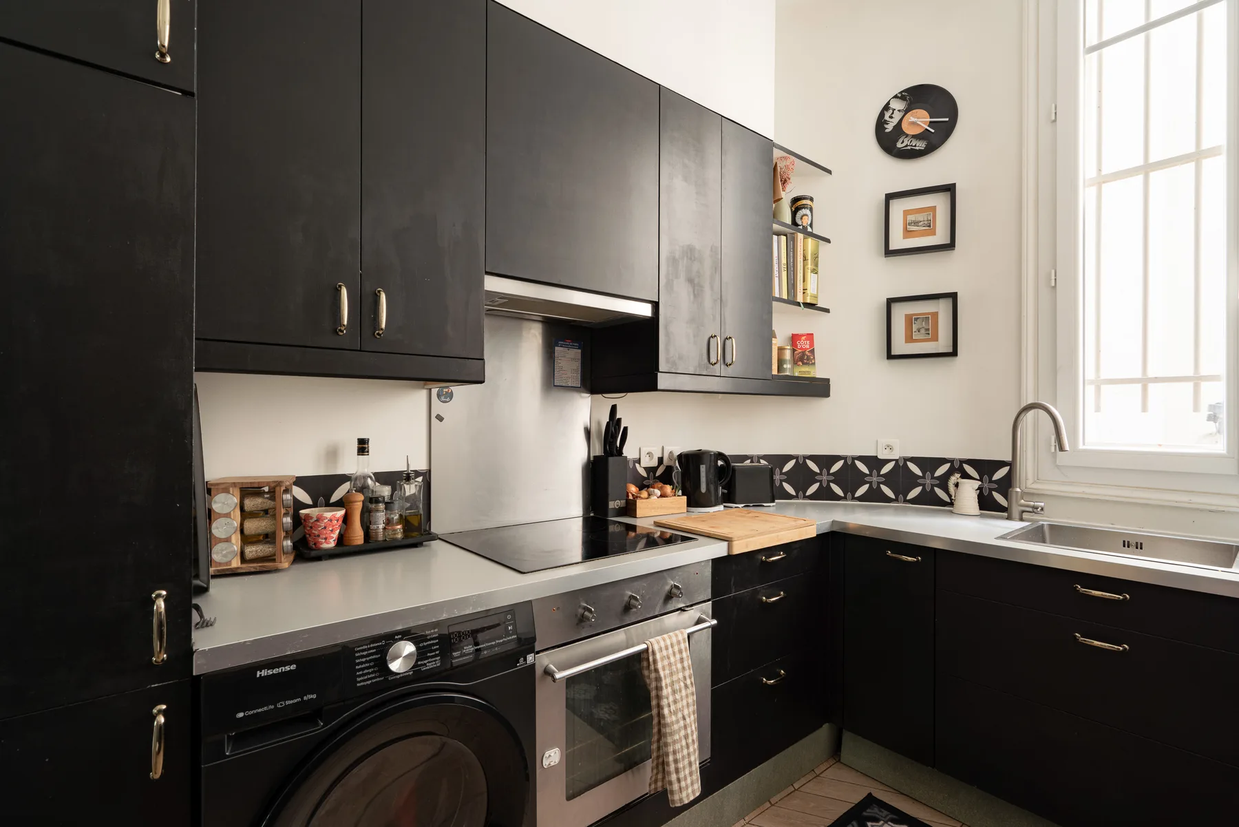 Una cocina con gabinetes oscuros, encimera, estufa y fregadero bajo una ventana luminosa.