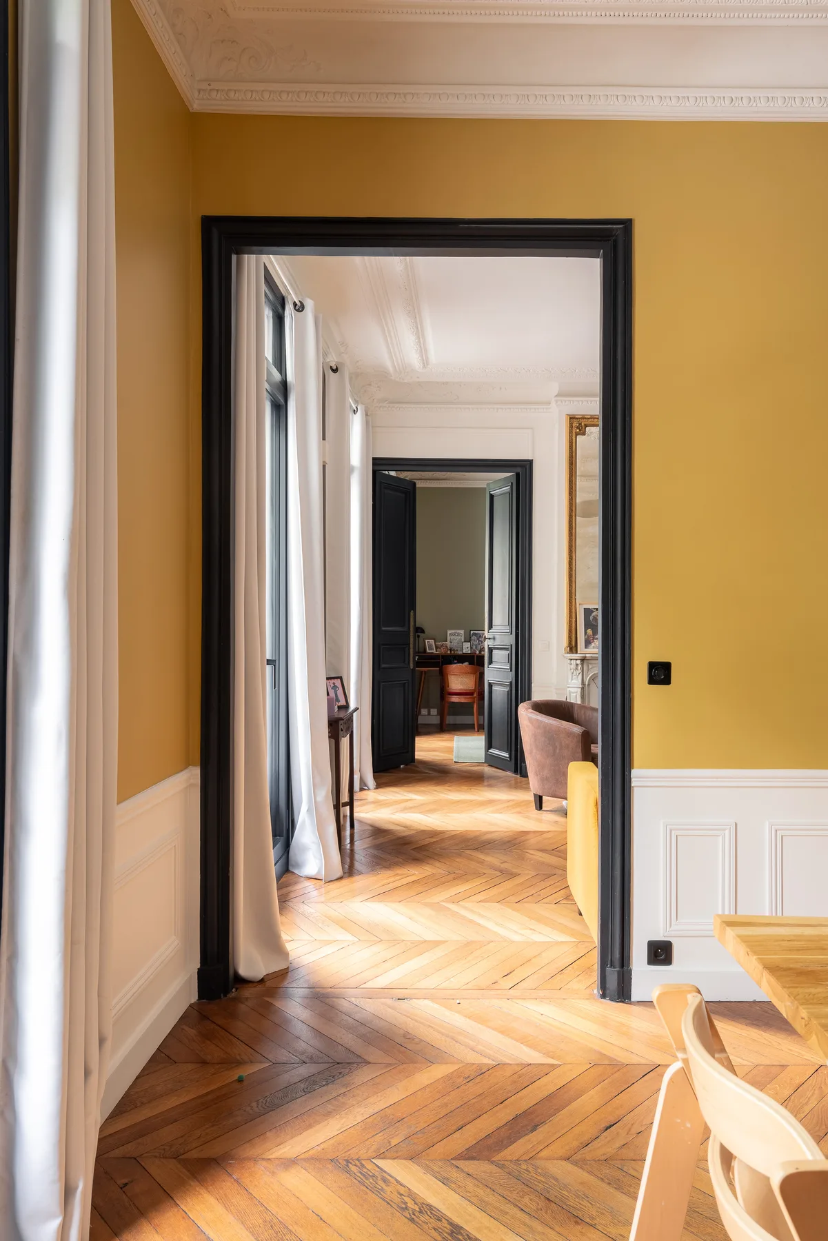 Un pasillo interior de color mostaza se abre a una habitación luminosa con suelo de madera.