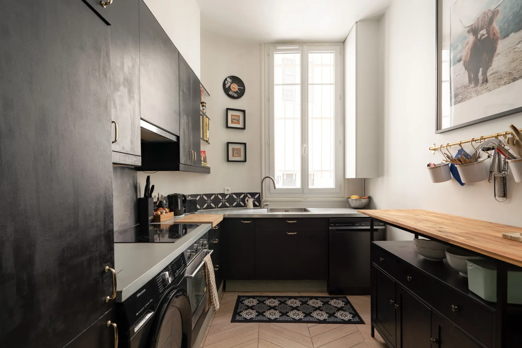 Una cocina estrecha con gabinetes oscuros, una ventana central y una encimera de madera.