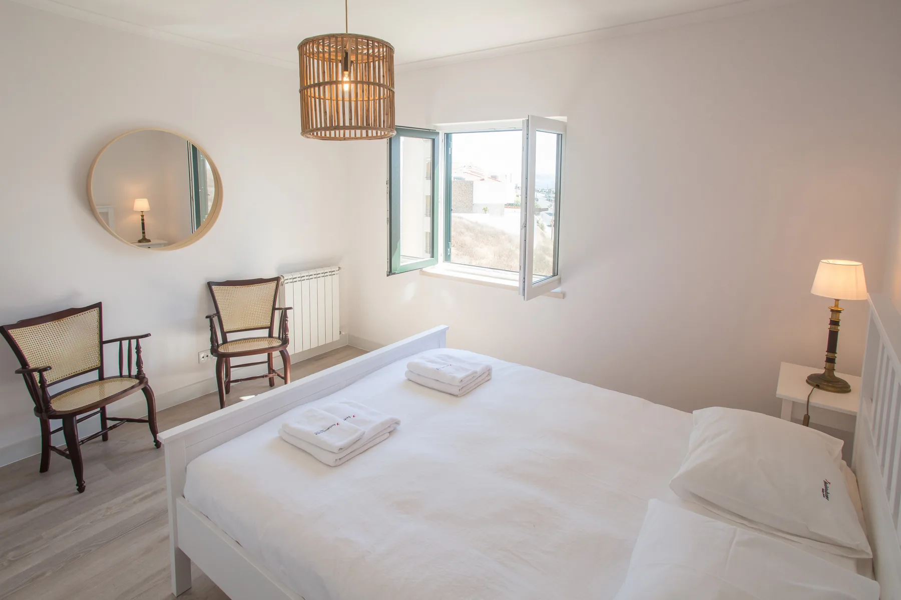 Un dormitorio luminoso con una cama blanca y una ventana abierta.