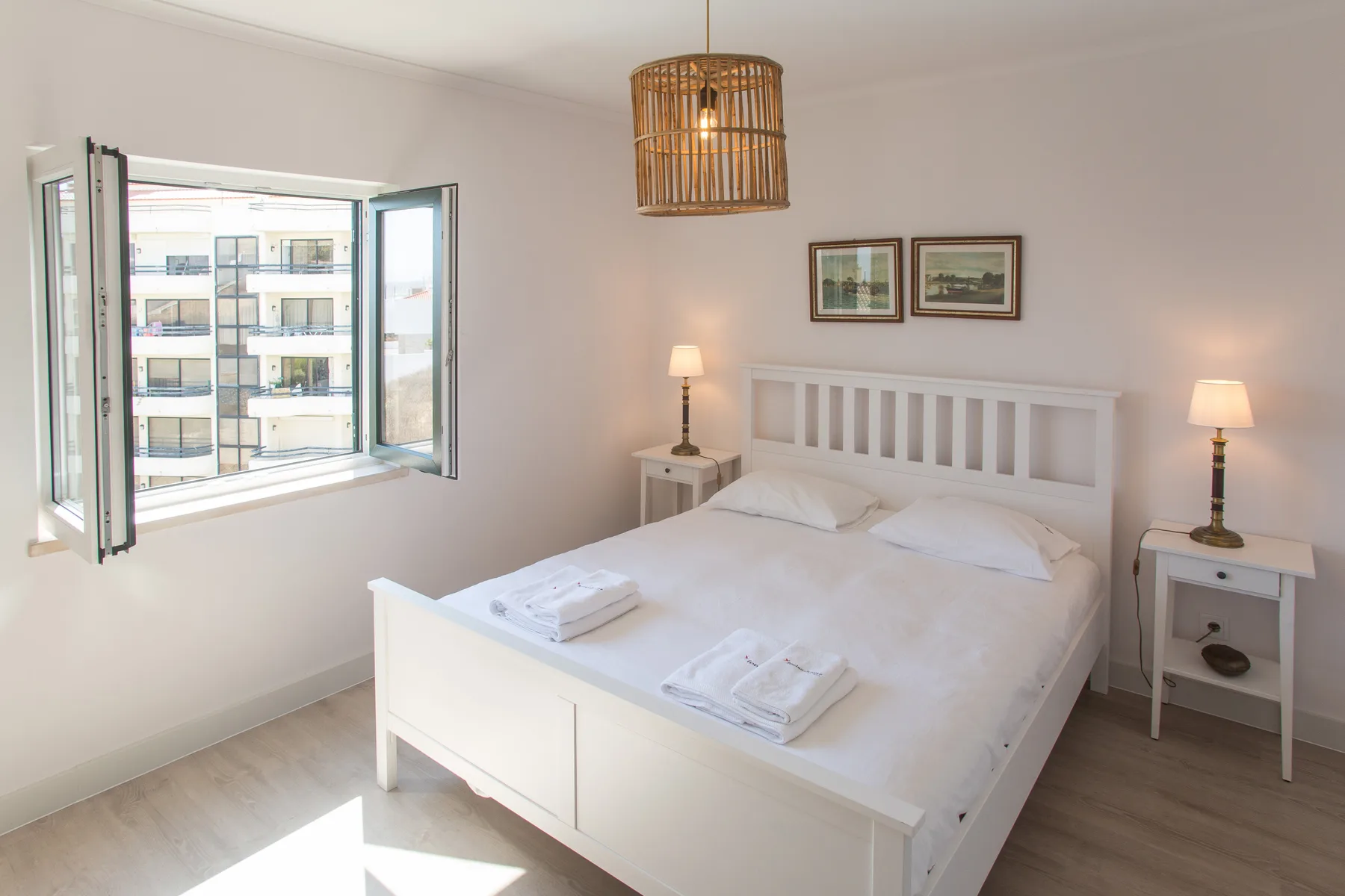 Un dormitorio luminoso con una cama blanca y una ventana abierta.