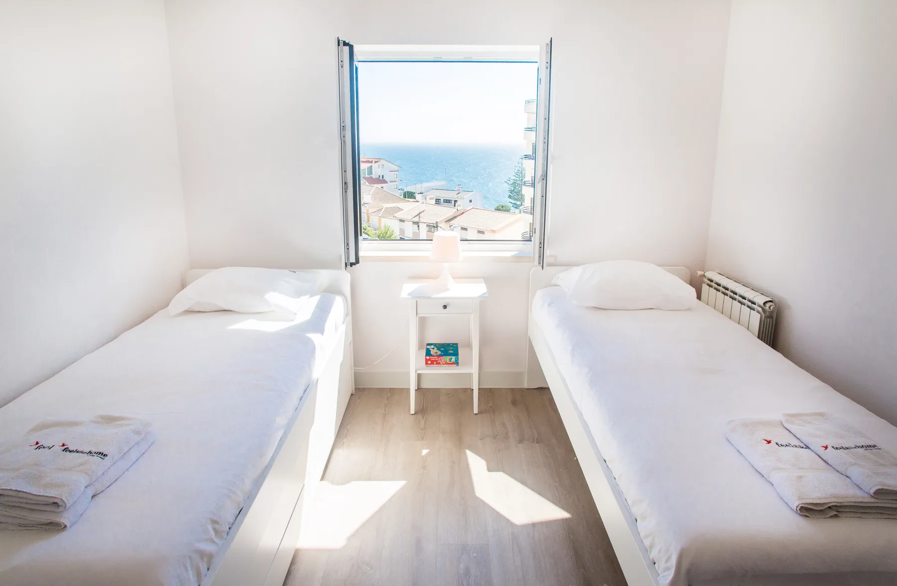 Un dormitorio luminoso con dos camas individuales y vistas al mar desde la ventana.