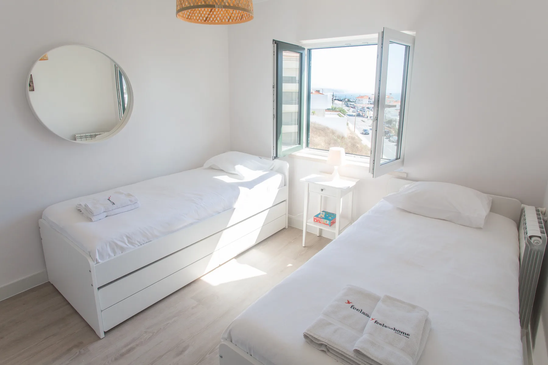 Un dormitorio luminoso con dos camas y una ventana abierta con vistas a la costa.