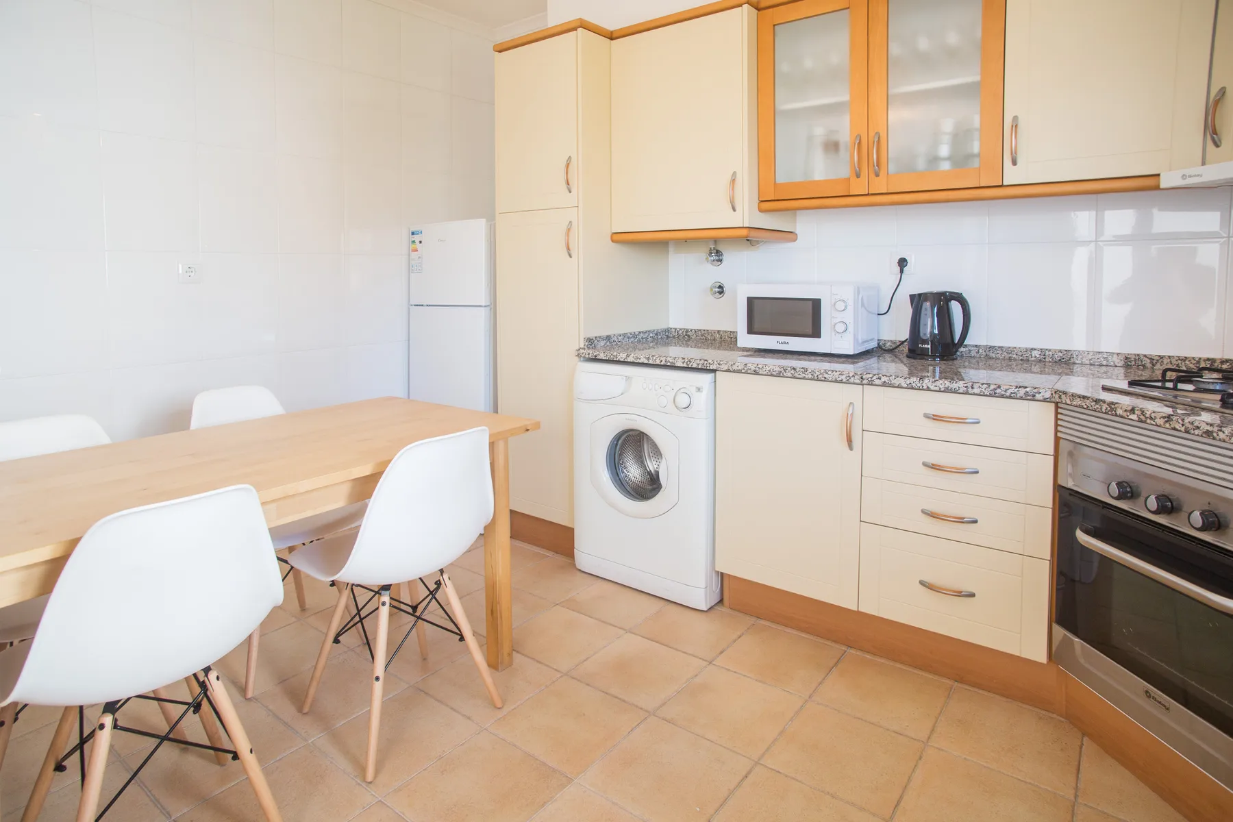 Una cocina y comedor luminosos con una mesa de madera y armarios blancos.