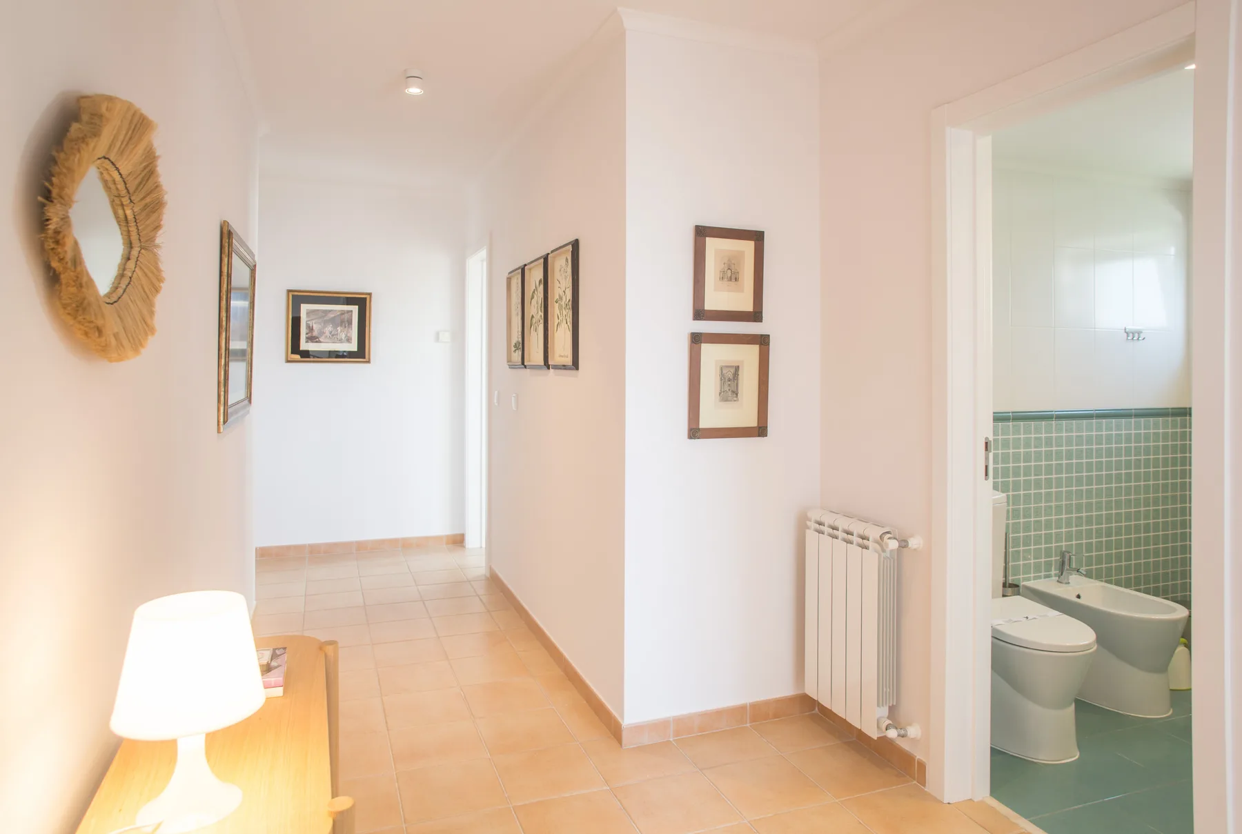 Un pasillo luminoso del apartamento conduce a un baño con azulejos verdes.