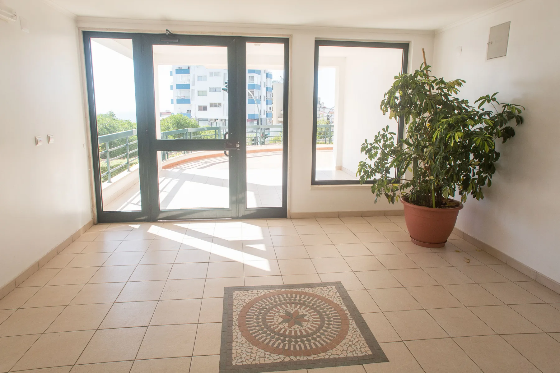 Una habitación luminosa con suelo de baldosas da a un balcón por puertas de cristal.