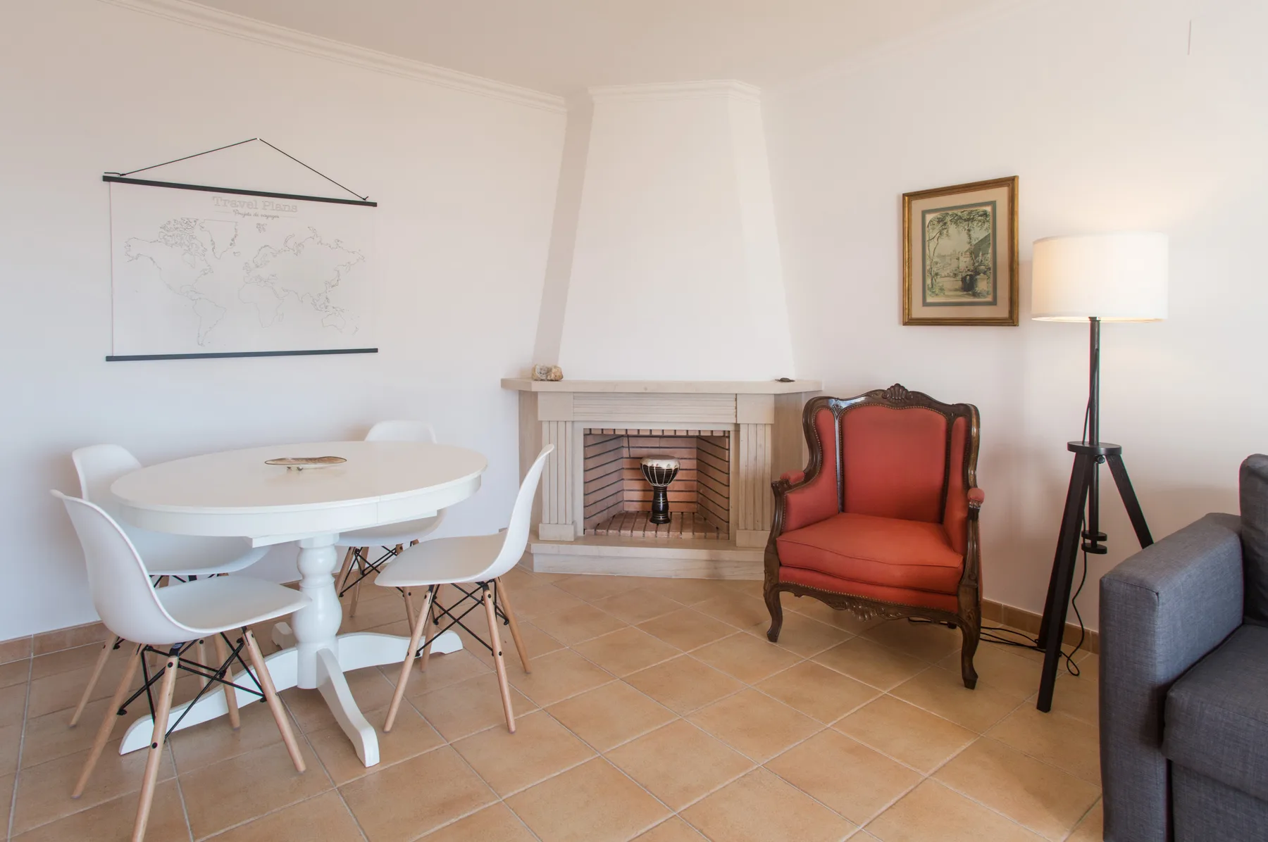 Zona de estar y comedor con una mesa blanca, una chimenea y un sillón rojo.