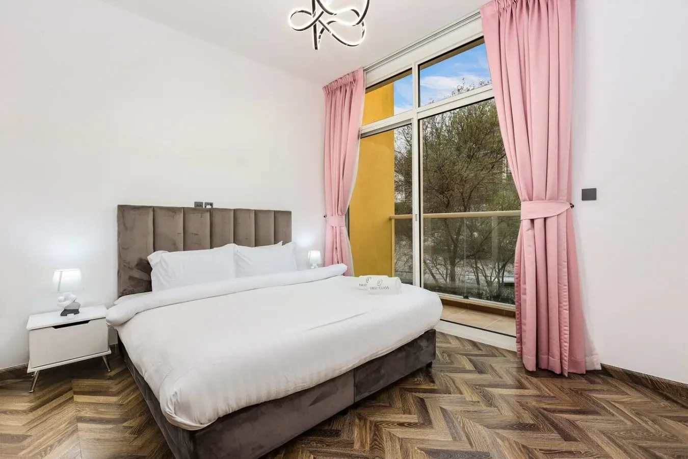 Un dormitorio con una cama junto a una gran ventana enmarcada por cortinas rosas.