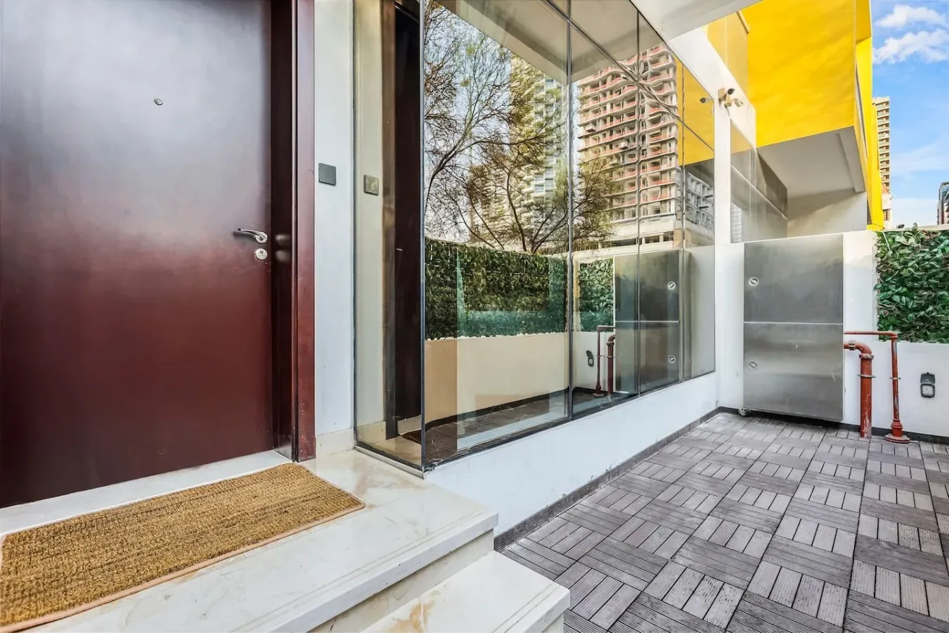Una entrada exterior pavimentada junto a una pared de vidrio y una puerta oscura.