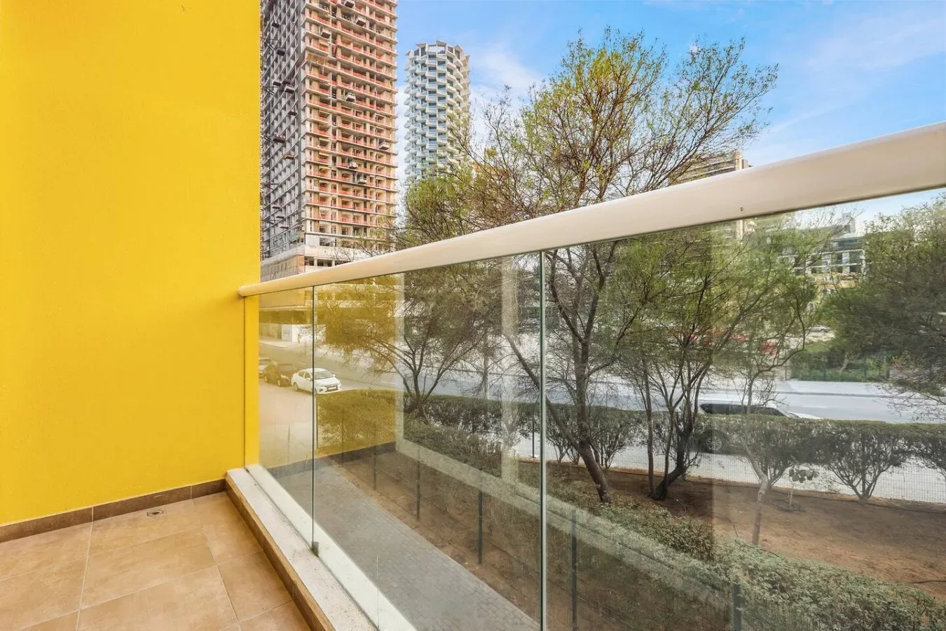 Un balcón con barandilla de vidrio da a árboles y edificios cercanos.