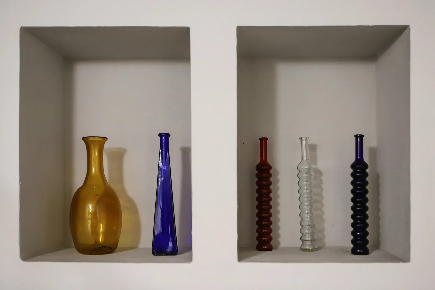 Dos nichos empotrados en la pared exhiben varias botellas de vidrio de colores.