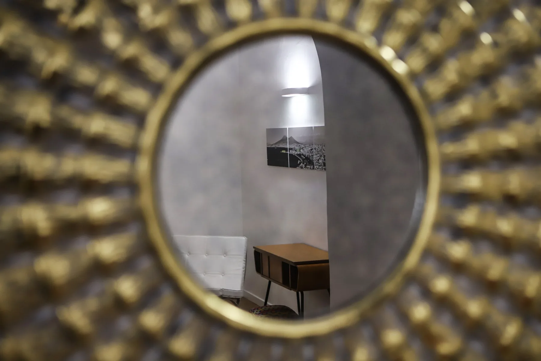 Un espejo decorativo redondo refleja un escritorio y una obra enmarcada en una habitación.