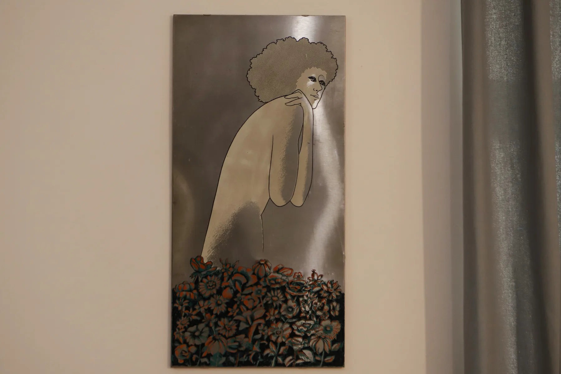 Un retrato enmarcado cuelga de una pared clara junto a una cortina gris.
