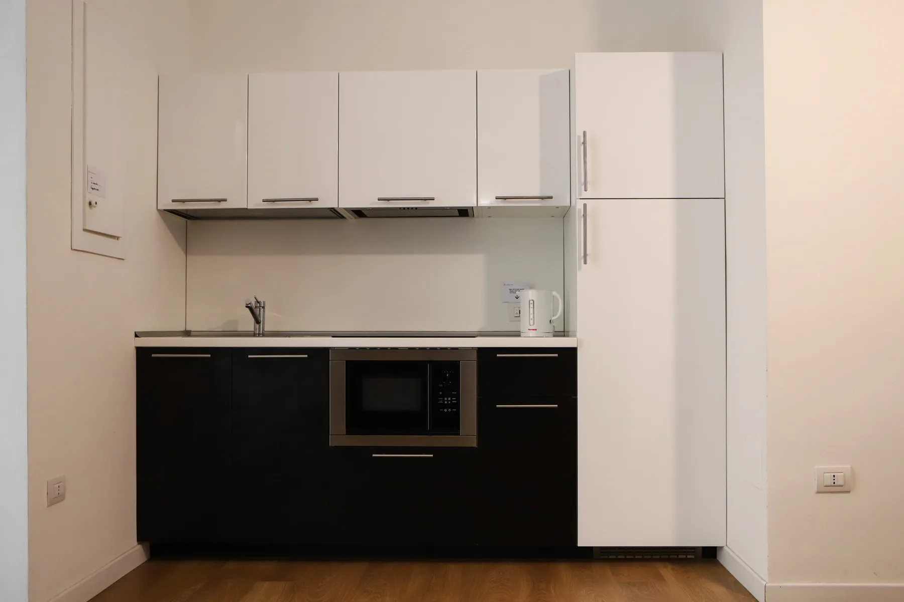 Una cocina compacta con armarios blancos, muebles bajos oscuros y un microondas integrado.