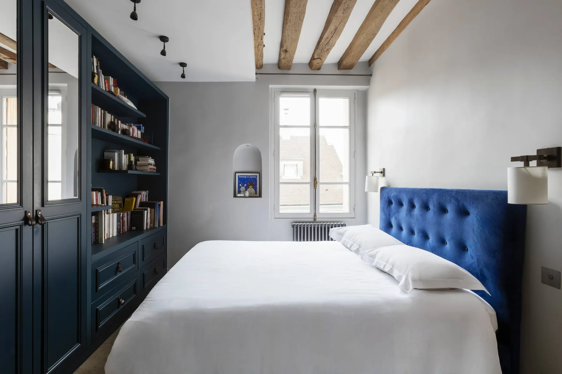 Un dormitorio luminoso con una cama y una estantería empotrada oscura.