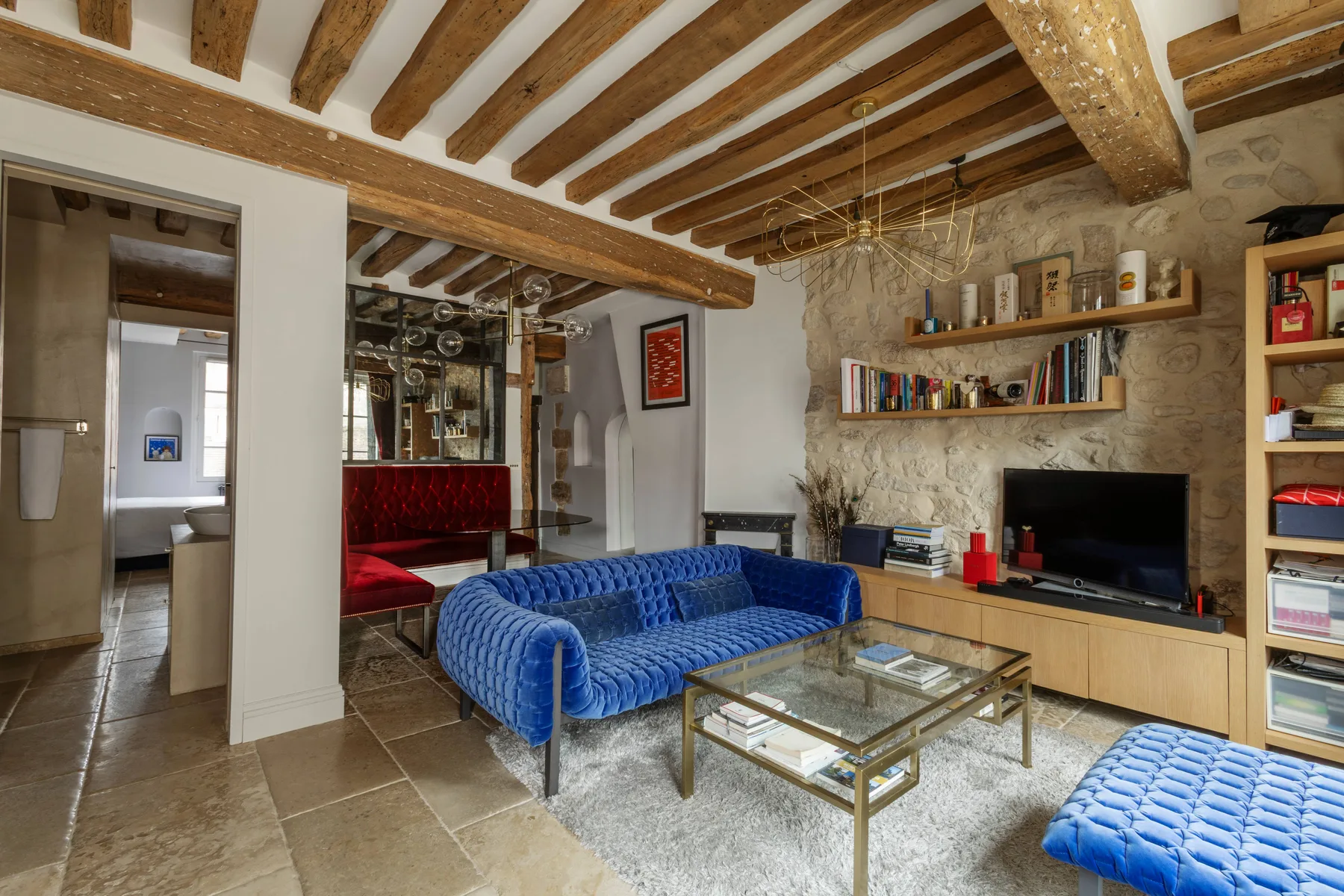 Una sala de estar con asientos azules, una mesa de centro de vidrio y un televisor.