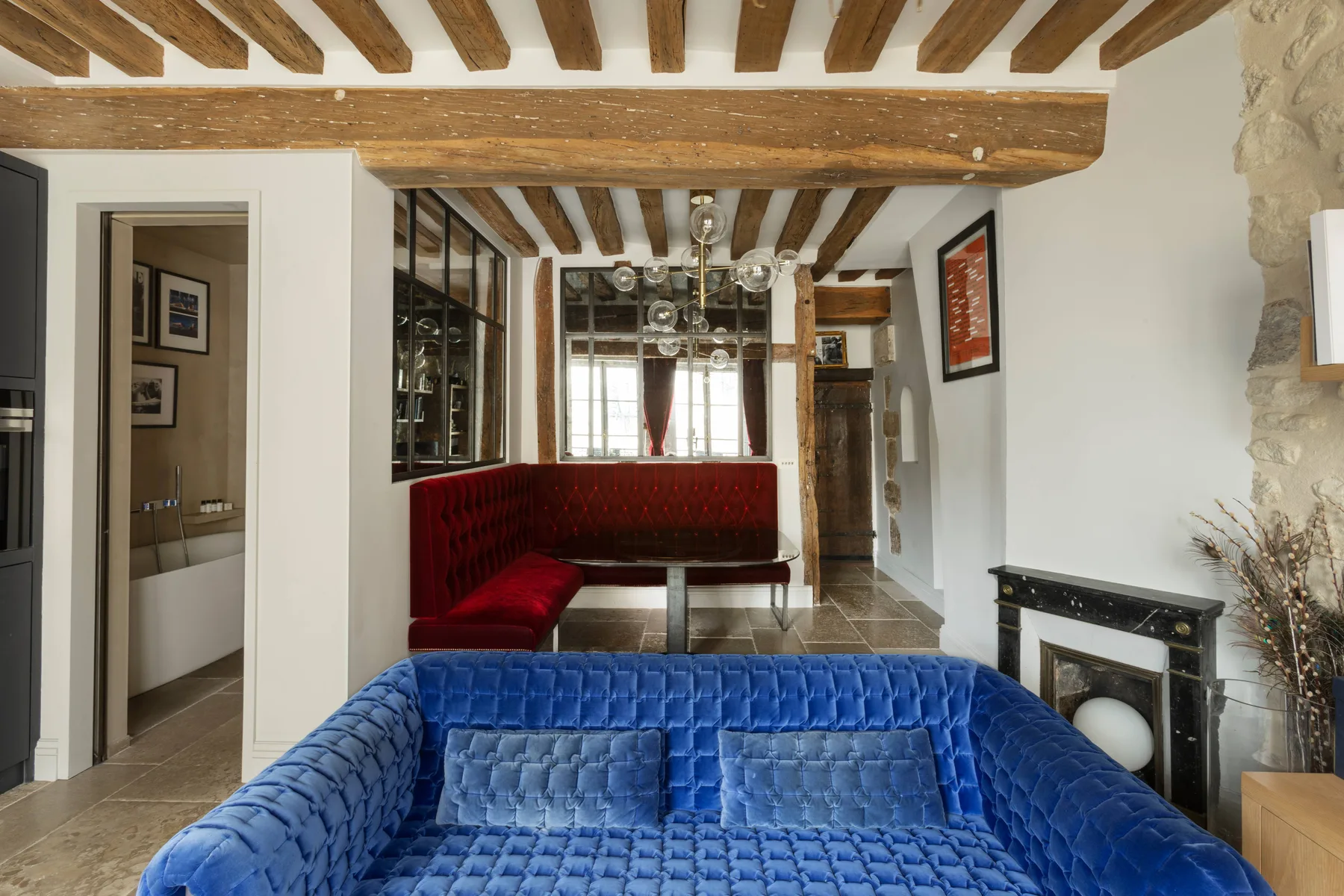 Una sala de estar con asientos azules en primer plano y una banqueta roja al fondo.