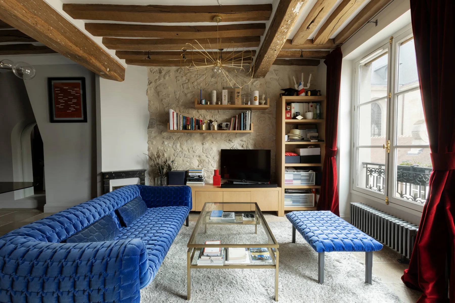 Una sala de estar con asientos azules, una mesa de centro de vidrio y una pared de piedra.
