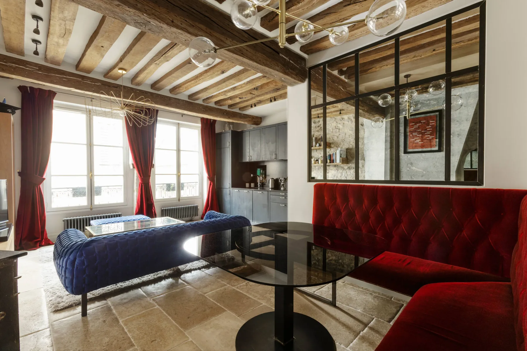Sala de estar con asientos rojos, una mesa de vidrio y vigas expuestas en el techo.
