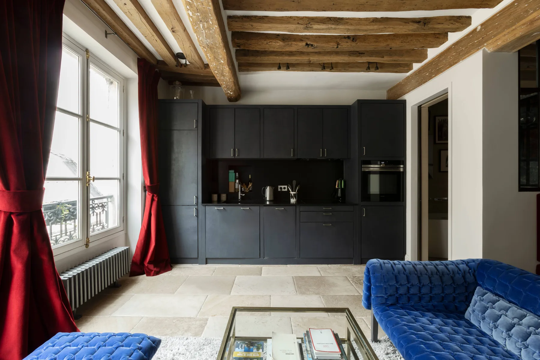 Una cocina moderna y zona de estar con gabinetes oscuros y vigas de madera a la vista.