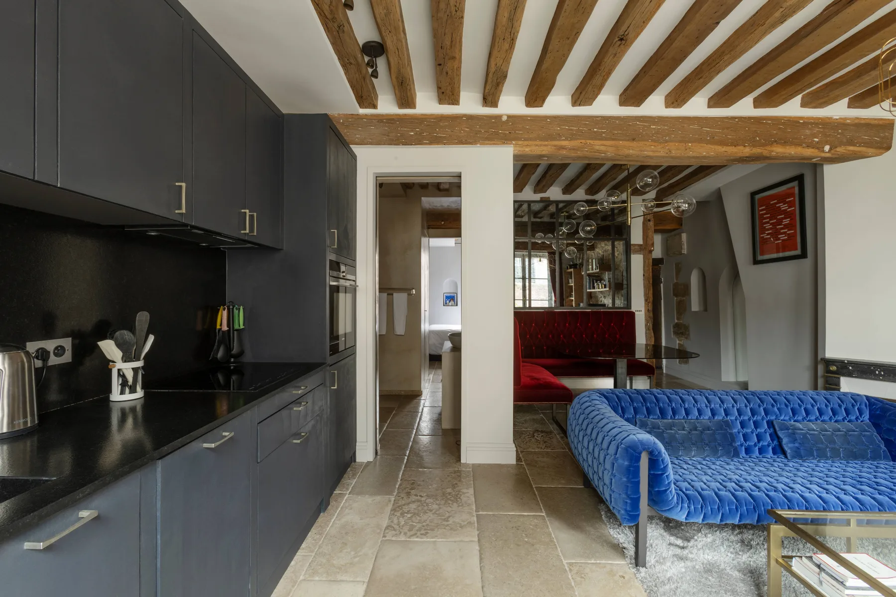 Una sala de estar moderna con asientos azules junto a una cocina oscura.