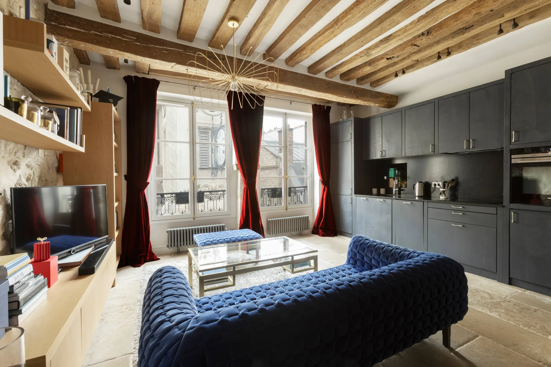 Una sala de estar con asientos oscuros, una mesa de centro de vidrio y ventanas altas con cortinas.