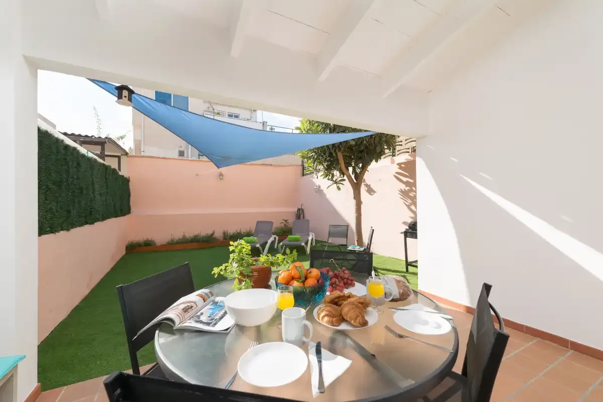 A covered outdoor dining area opens onto a small patio with a shade sail.