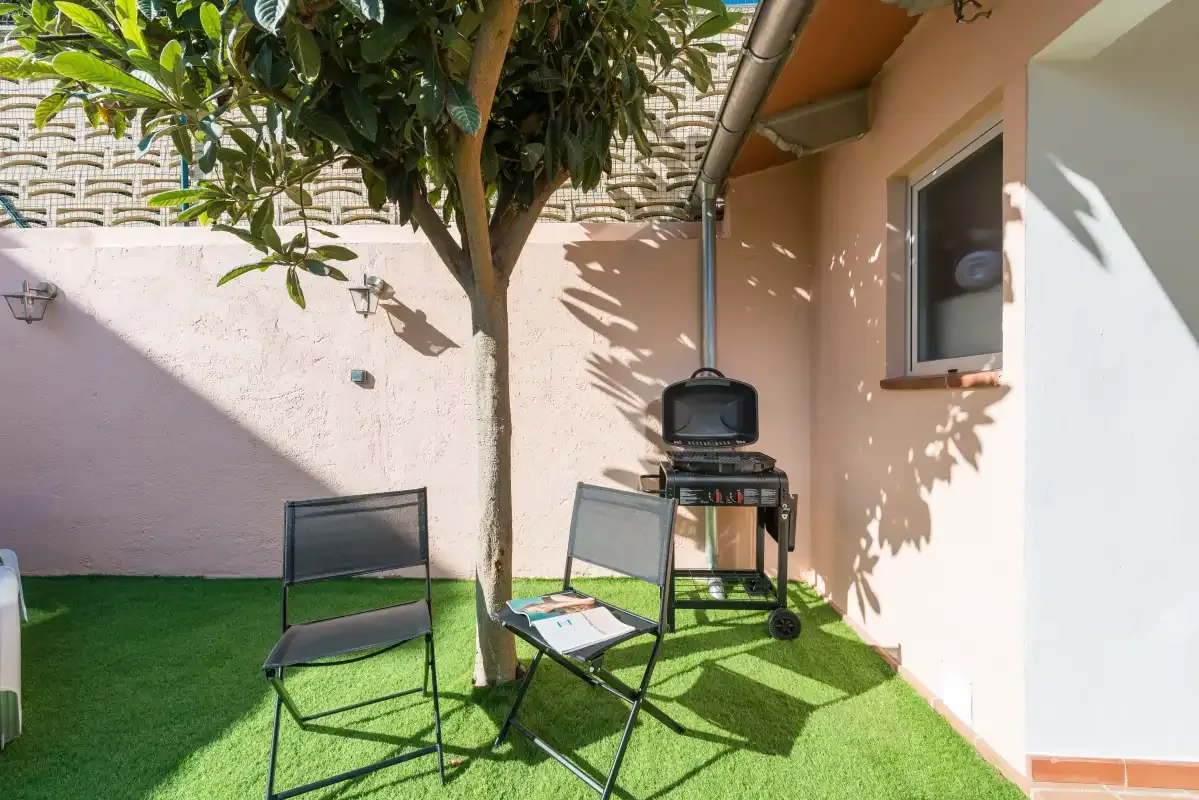 A small outdoor patio has artificial grass, folding seating, and a barbecue.