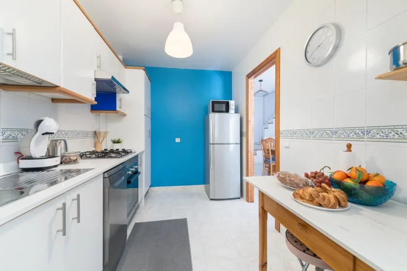A bright kitchen with white cabinets, a refrigerator, and a blue accent wall.