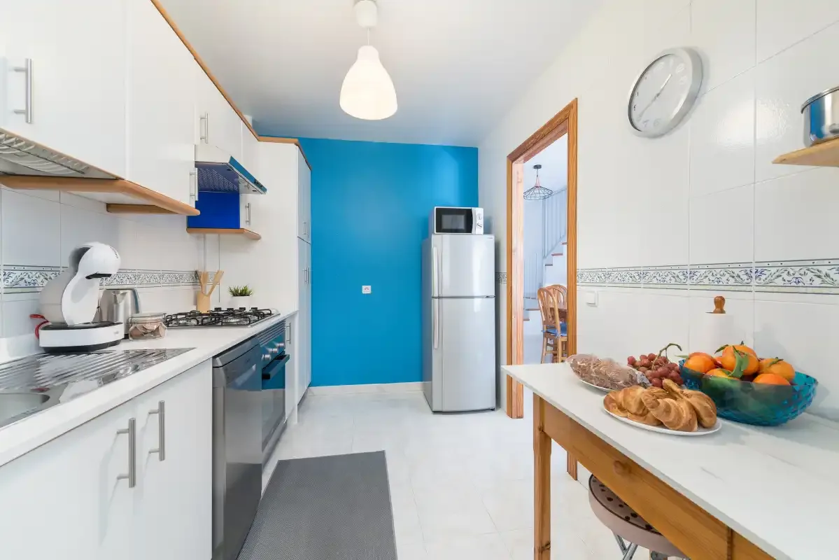 A bright kitchen with white cabinets and a turquoise accent wall.