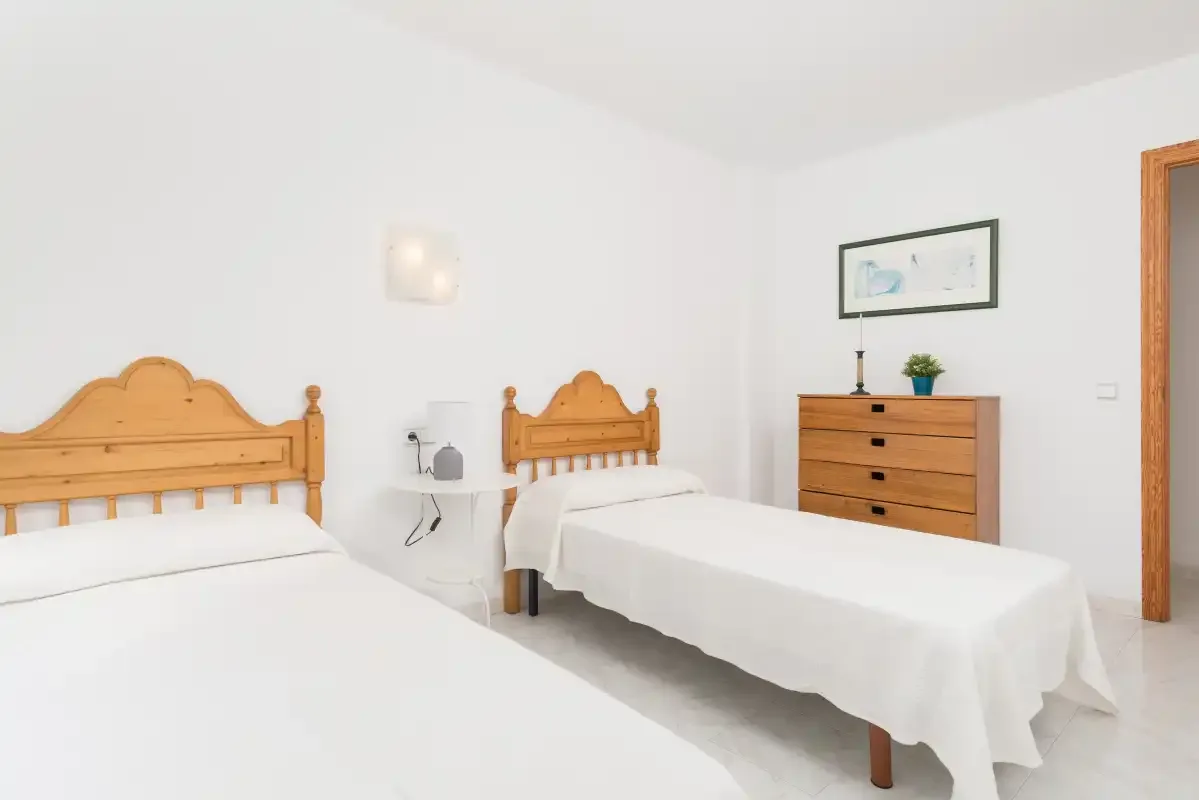 A bright bedroom with two beds and a wooden dresser.