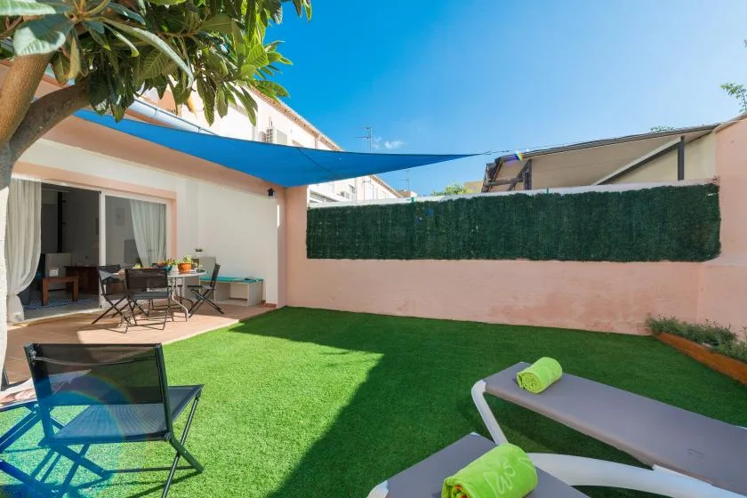 A sunny outdoor patio with green lawn, shaded seating, and a fabric canopy.