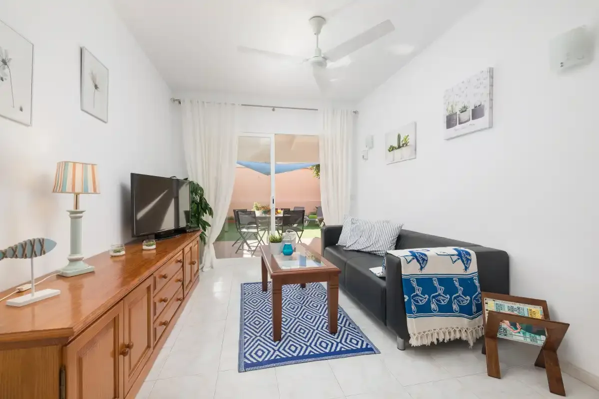A bright living room with seating and a glass door opening onto a balcony.