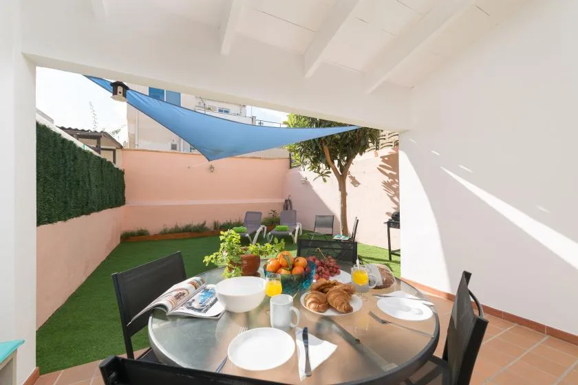 A covered outdoor dining area opens onto a small garden with a shade sail.