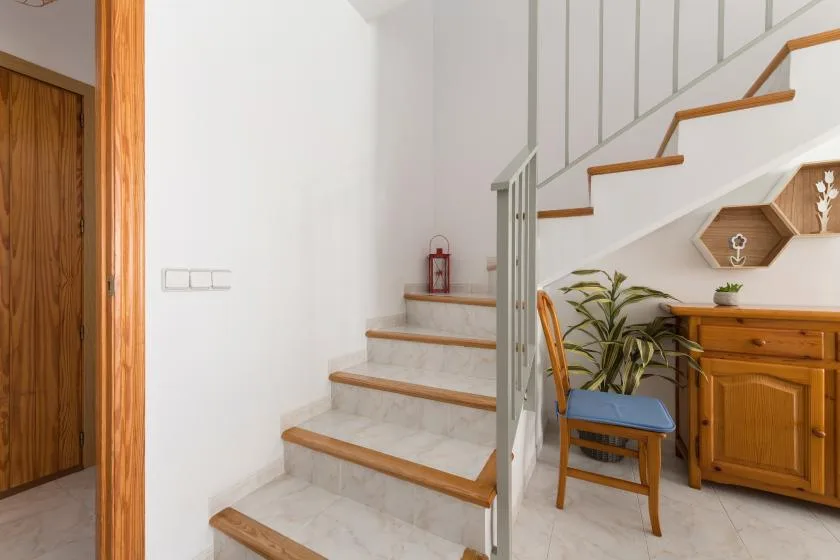 A bright interior staircase with a wooden cabinet and chair beside it.