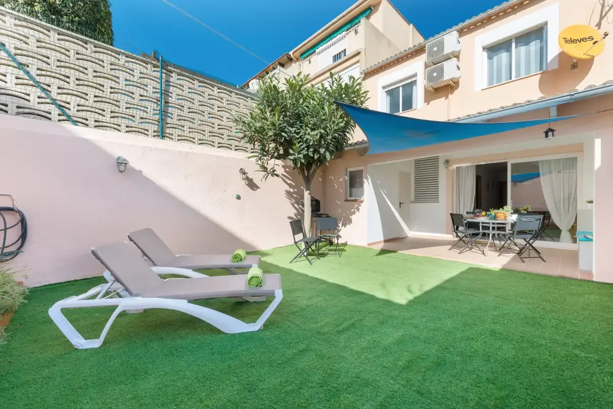 A furnished patio with artificial grass, loungers, and a dining area beside the house.