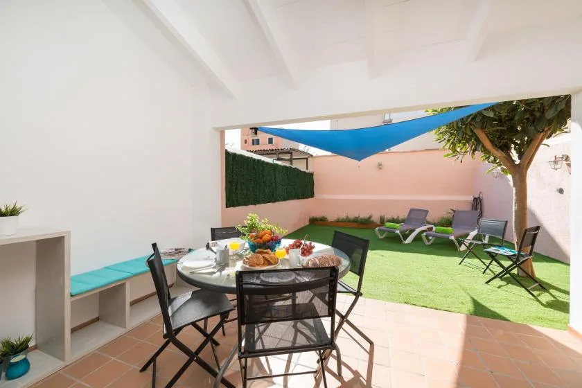 A shaded outdoor dining area opens onto a small lawn with lounge seating.