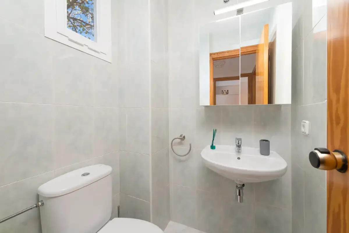 A tiled bathroom with a toilet, sink, and wall mirror.
