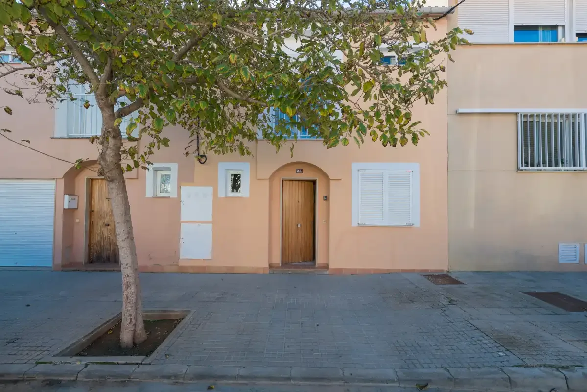 A peach-colored building facade with wooden doors and windows beneath a leafy tree.