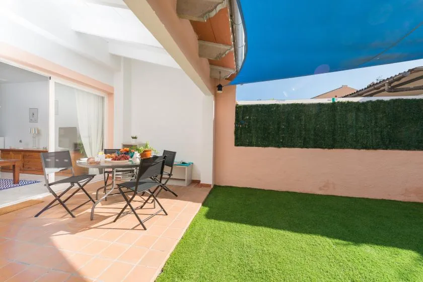 A patio dining area beside a small green lawn under a blue awning.