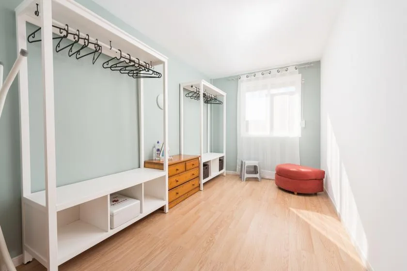 A bright dressing room with open clothes rails, storage drawers, and a window.