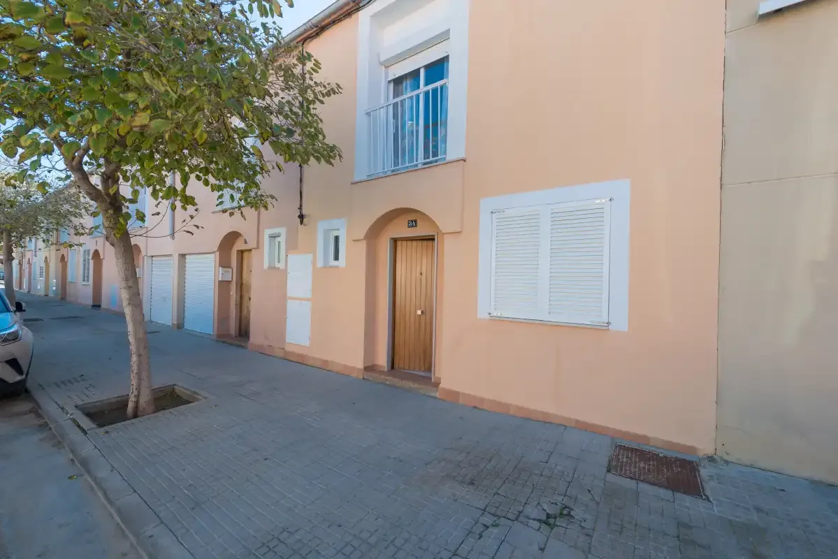 A peach-colored building entrance opens onto a paved street beneath a leafy tree.