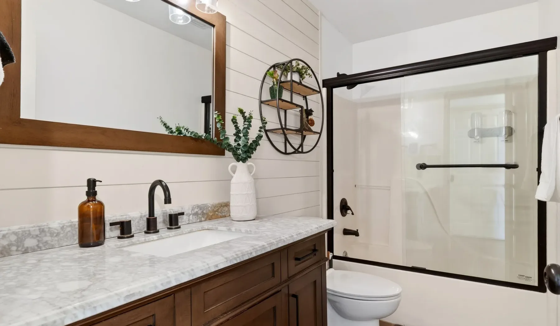 Un tocador de baño con encimera de aspecto marmolado está junto a una ducha de vidrio.