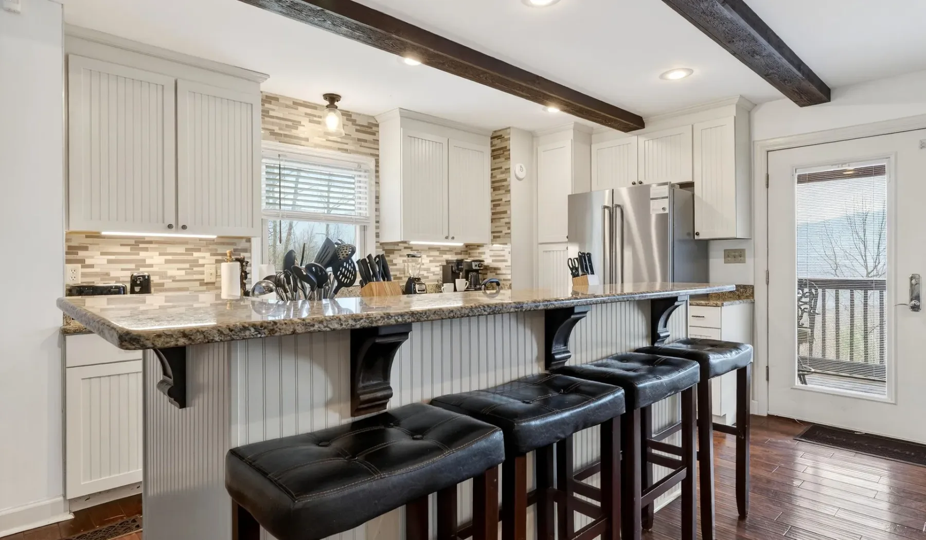 Una cocina luminosa cuenta con una isla larga con asientos y gabinetes blancos.